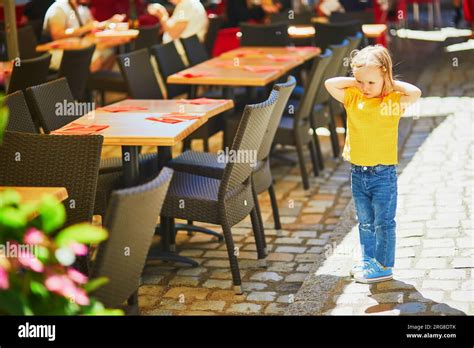 Unhappy and stubborn toddler girl in outdoor restaurant. Misbehaving child outdoors. Terrible ...