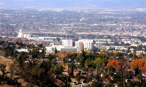 a city with mountains in the background and trees on the hillside, near an orange fire hydrant