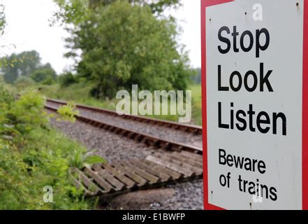 Unmanned pedestrian railway crossing footpath warning signs and passing train South eastern ...