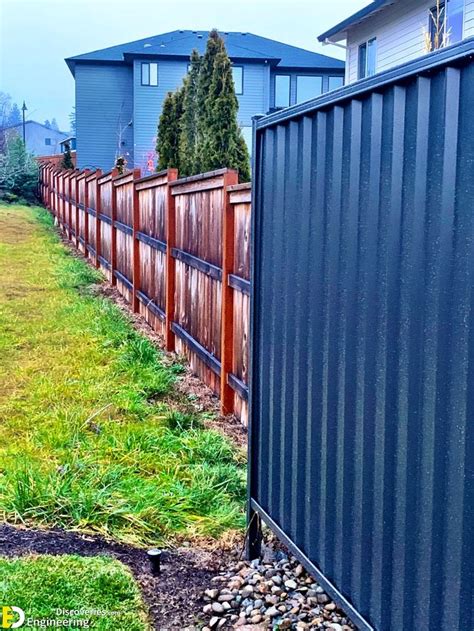 a row of houses behind a fence with grass and rocks on the ground next ...