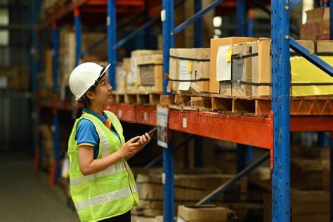 Female Warehouse Worker Wearing Hardhats and Reflective Jackets Checking Inventory Boxes with ...