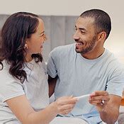 Excited couple, bed and positive pregnancy test for family, start or maternity at home. Face of ...