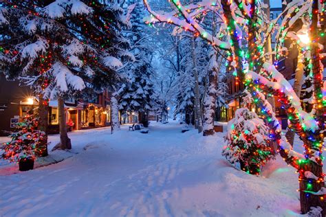 Download A Snowy Street With Christmas Lights And Trees | Wallpapers.com