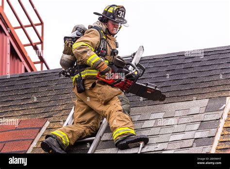 Firefighter standing on a roof during with a saw during firefighter ...