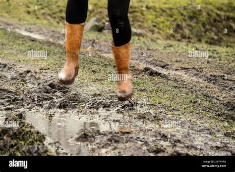 woman jumping in the puddle of mud in autumn with orange rubber boots ...