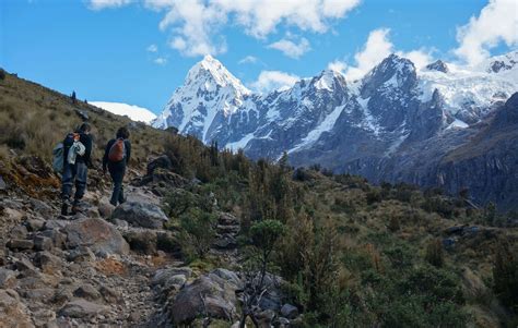 two hikers trekking up a rocky trail with snow capped mountains in the background