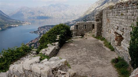 an old stone building on the side of a mountain overlooking a body of water with mountains in ...