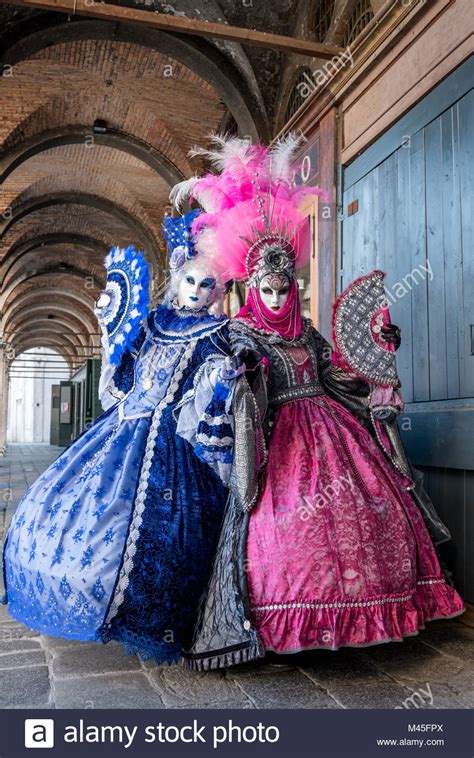 Two women holding fans and wearing hand painted masks and ornate costumes under the arches at ...