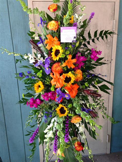 Colorful standing funeral Spray with sunflowers, orange roses and lilies with purple garden ...