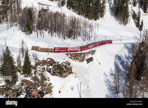 Aerial view of the red Bernina train coming from Bernina Pass in winter ...