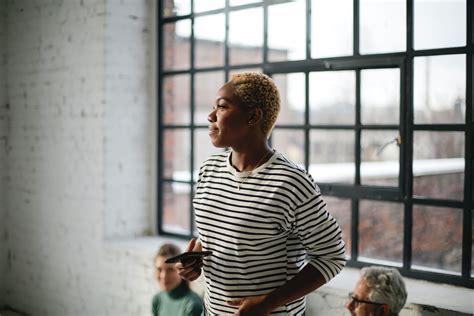 Smiling black woman with smartphone standing in loft styled studio · Free Stock Photo