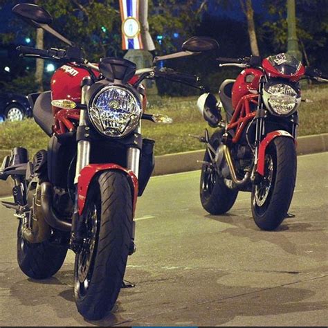 two motorcycles parked next to each other on a street at night time with lights in the background