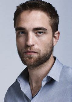 a man with a beard and blue shirt looking at the camera while standing in front of a white ...