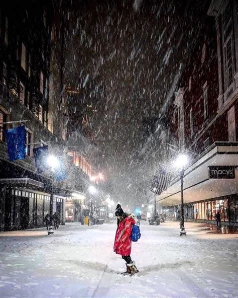 a person is standing in the middle of a snowy street at night with their back to the camera