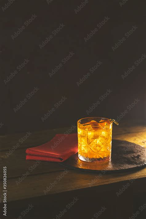 Glass of the cocktail negroni with red napkin and black stone tray on a old wooden board. Drink ...