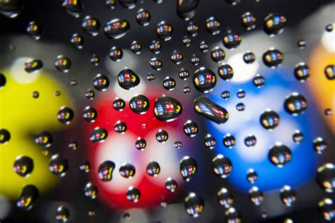 Water droplets on hydrophobic waxed acrylic form lenses in which Pacman shot glasses are focused ...