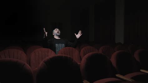 Jubilant Audience Member in Empty Theater, Man with beard, joyfully raising arms in an empty red ...