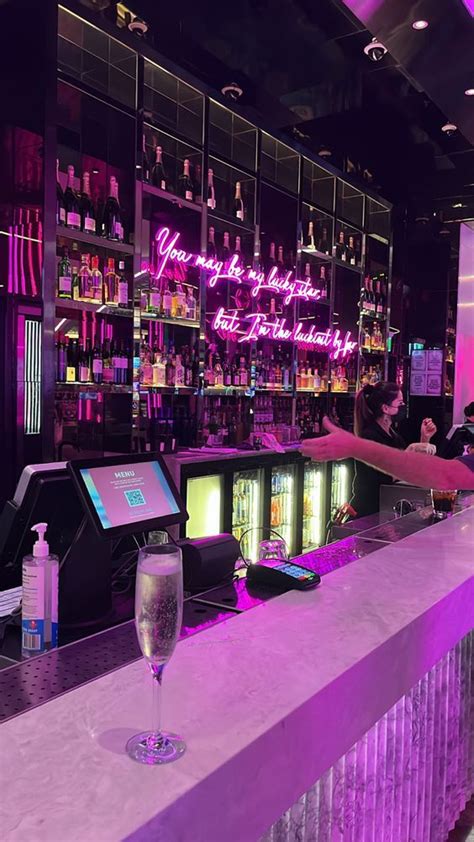 a bar with purple lighting and neon signs on the back wall, along with ...