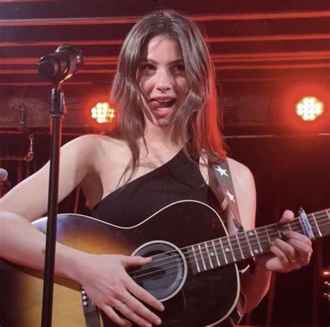 a woman singing into a microphone while holding an acoustic guitar