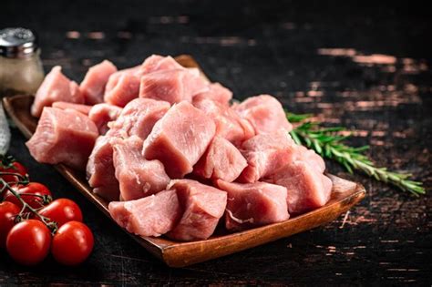 Premium Photo | Pieces of raw pork on a wooden plate with spices and tomatoes