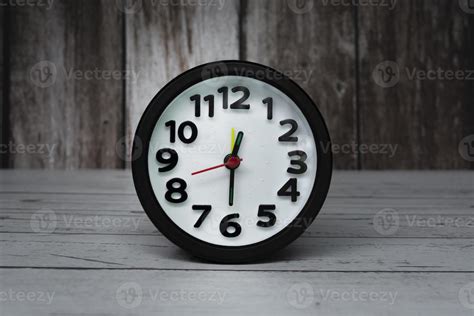 Black alarm clock isolated on wooden desk. The clock set at half past ...