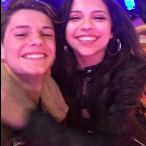 two people are smiling and posing for the camera at a bar with lights in the background