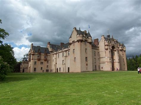 an old castle with people standing in front of it on a grassy field ...