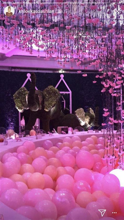 pink and white balloons are floating in the air above a table filled with tables, chairs and ...