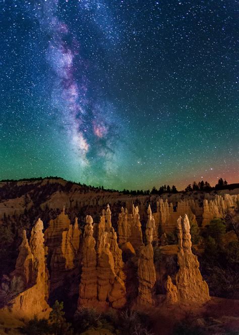 the night sky is filled with stars above hoodoos and trees in the ...