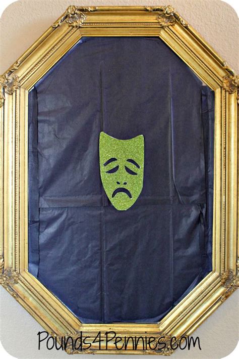 a mirror with a green mask on it in front of a white wall and gold frame