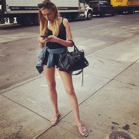 a woman is standing on the sidewalk looking at her cell phone and holding a purse