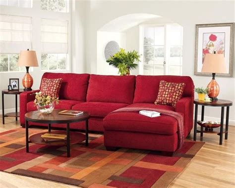 a living room with red couches and rugs on the wooden floor, two end tables