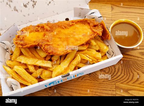 Fish and chips served with curry sauce at Tynemouth in England. The dish is traditional British ...