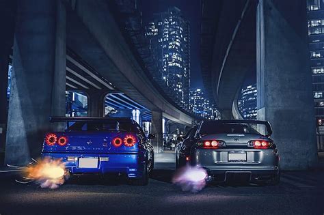 two cars on the road at night with city lights in the background