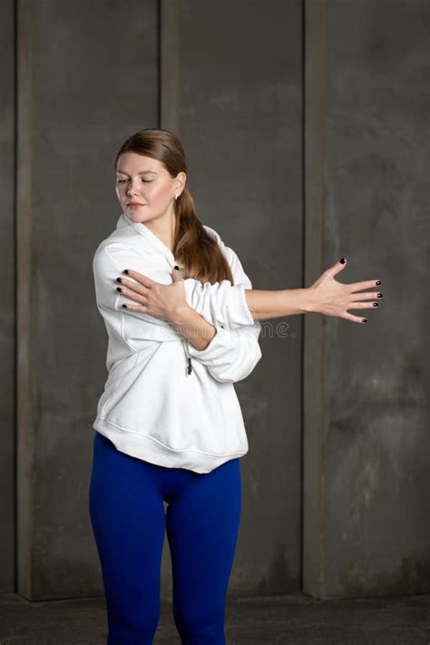 An Athlete in Leggings and a Hoodie Stretches Her Arm, Warming Up the Shoulder Muscles ...