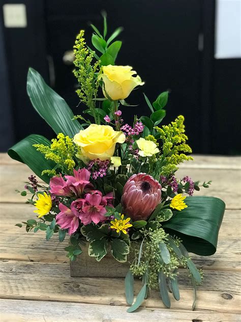 a bouquet of flowers sitting on top of a wooden table with greenery and yellow roses