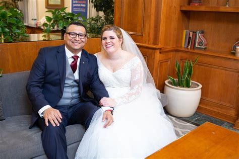 a bride and groom sitting on a couch in front of bookshelves at a library