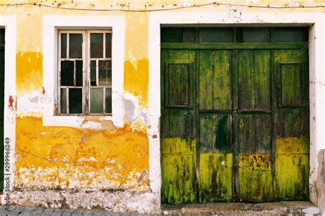 Photograph of an old garage door in green painted wood. Wall painted with peeling yellow paint ...