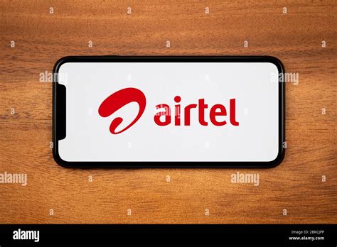 A smartphone showing the Bharti Airtel logo rests on a plain wooden table (Editorial use only ...