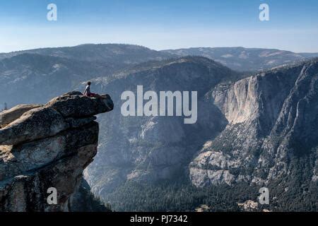 A sits on an overhanging rock at Glacier Point enjoying the ...