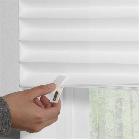 a hand holding a remote control in front of a window with white blinds on it