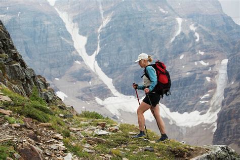 Female hiker with poles hiking up mountain path with mountain cliff ...