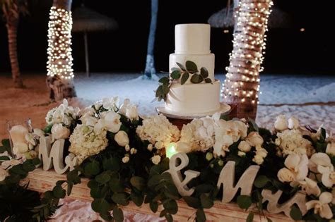 a white wedding cake sitting on top of a table covered in flowers and ...