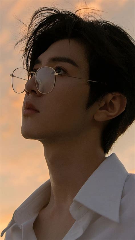 a man wearing glasses looking off into the distance with clouds in the ...