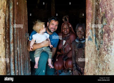 White tourist with his baby in a Himba village with Himba people ...