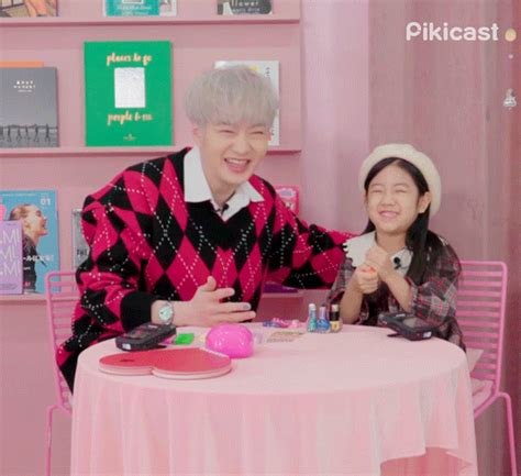 two people sitting at a table in front of pink walls with books on the shelves