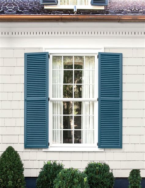 an open window with blue shutters on the side of a white brick building ...