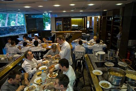 a group of people sitting at tables eating food in a large room with an aquarium on the wall