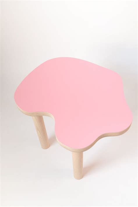 a pink table with wooden legs on a white background in the shape of an egg