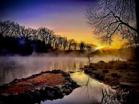 the sun is setting over a body of water with trees in the foreground ...